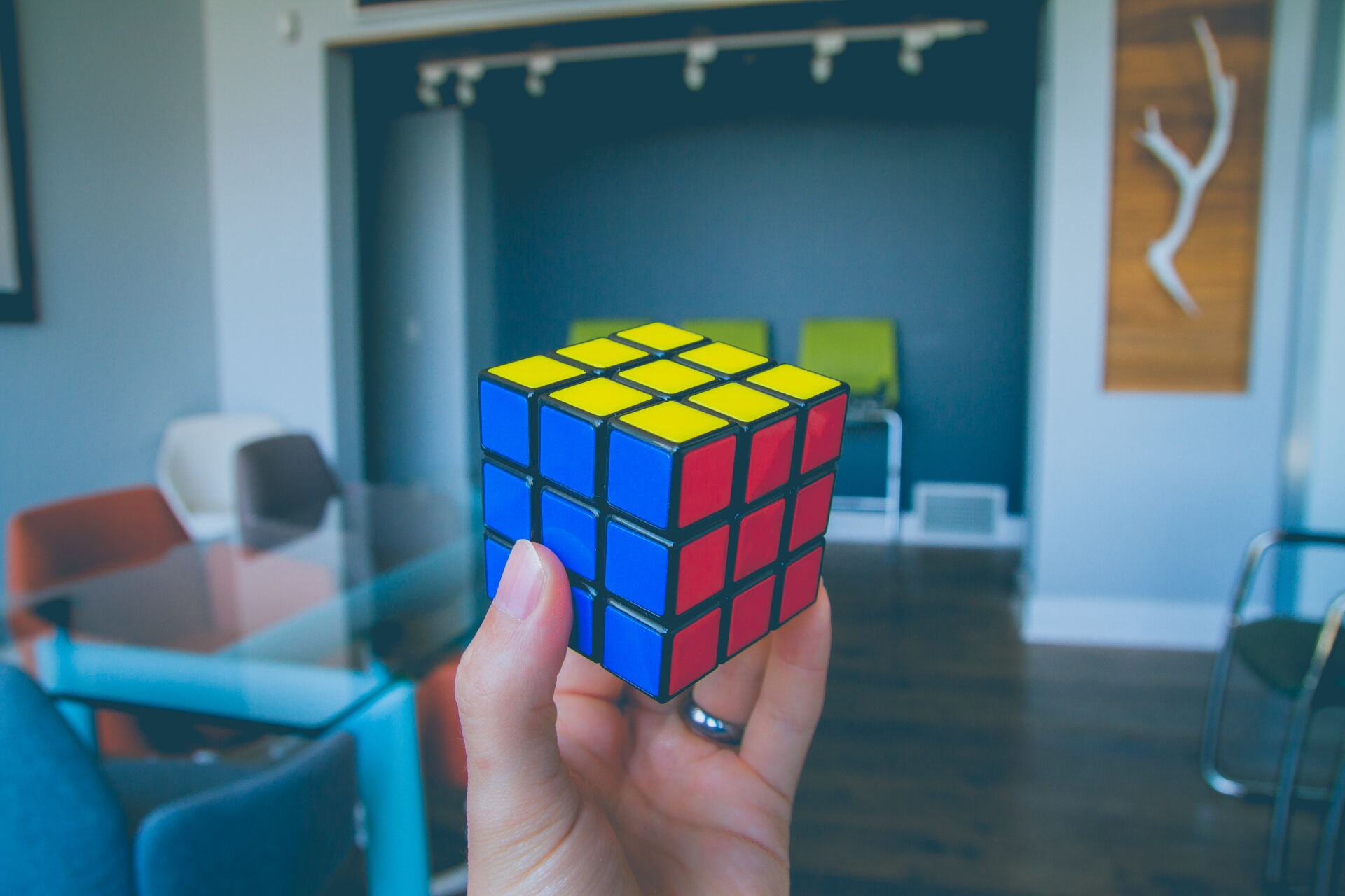 A hand holding a solved Rubik's cube against a modern studio office